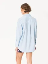 Camisa de poplin rayada rosa y celeste, de corte holgado, con cuello clásico, cierre frontal con botones y bolsillo plaqué en el pecho.