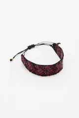 Pulsera tejida con pequeñas cuentas de vidrio rojas y negras, con cierre ajustable mediante cordones negros.