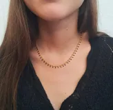 Collar dorado con cadena fina y pequeños colgantes negros.