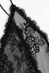 Top negro de breteles finos, confeccionado en encaje floral transparente. Presenta escote en V con botones forrados al frente, un ribete de volados bajo el busto y un segundo volado doble en el bajo.