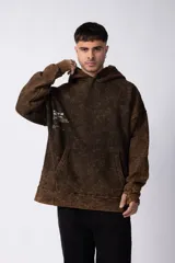 Buzo canguro negro con capucha, de corte oversize y estética lavada. Presenta un bolsillo tipo canguro y puños con orificio para el pulgar. Estampado con texto en el lateral izquierdo.