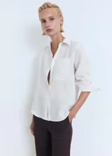 Camisa blanca de lino con cuello camisero, manga larga con puños abotonados, cierre frontal con botones y bolsillo de parche en el pecho.