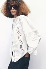 Camisa blanca de cuello redondo y manga larga con bordados combinados a tono y cierre frontal con botones.