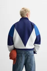 Chaqueta deportiva azul marino, azul y blanca con cierre frontal, cuello alto y bolsillos laterales.