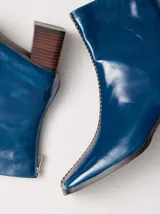 Botas de cuero charol negro con caña media y punta cuadrada. Cuentan con cierre trasero, tirador y bordado contrastante en el empeine. El taco es de madera y la suela de goma.