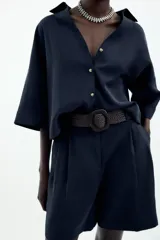 Camisa azul marino de cuello solapa con escote pico y manga ancha por debajo del codo con trabilla y botón. Cierre frontal con botones.