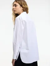 Camisa blanca de algodón con cuello camisero, cierre frontal con botones y tachas plateadas en el frente.