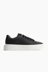 Zapatillas negras de cuero sintético con cordones negros y suela gruesa blanca.