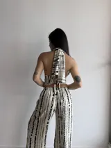 Top de cuello halter con escote en V profundo, confeccionado en tela slab con estampado de rayas abstractas negras sobre fondo beige. Se ajusta mediante lazos en el cuello y la espalda, con terminación en punta en la parte frontal.