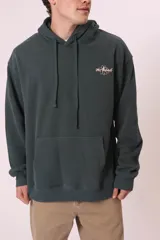 Sudadera con capucha de color verde oscuro (o verde petróleo) con efecto lavado, corte holgado y bolsillo canguro. Presenta un pequeño bordado blanco en el pecho con un diseño floral y texto.