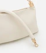 Cartera shoulder de poliuretano color crema, con asa corta de mano y asa larga de cadena dorada, ambas removibles. Incluye cierre de cremallera y borla decorativa.