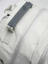 Mochila gris claro y gris oscuro con cordones elásticos cruzados en el frente y logo de la marca en la parte superior.