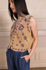 Chaleco color beige con bordados florales en tonos violeta y rosa, sin mangas y con cierre frontal con ganchos.