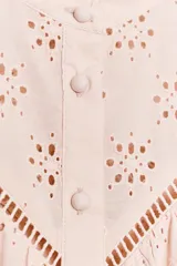 Camisa rosa pálido con bordados perforados, cuello con volante y mangas largas abullonadas. Cierre frontal con botones a tono.