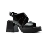 Sandalias negras de plataforma Korium con taco cuadrado, tira ancha sobre los dedos y tira cruzada de charol sobre el empeine. Ajuste con hebilla al tobillo.