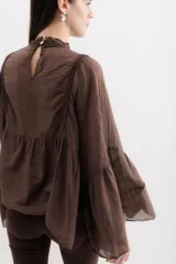 Camisa color marrón con cuello mao, mangas largas abullonadas y detalle de volados en el frente.