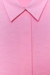 Camisa rosa de cuello solapa y manga corta con vuelta. Bajo asimétrico con aberturas laterales. Cierre frontal con botones ocultos por solapa.