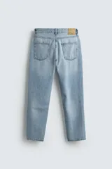 Jeans de denim de algodón, color negro lavado, con tiro medio, corte ajustado en cadera y muslos, y pierna que se estrecha hacia el tobillo. Presenta cinco bolsillos y cierre frontal con cremallera y botón.