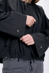 Campera negra corta con frunces en la cintura y cierre frontal.