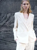 Blazer color crema con cuello de solapa, cierre cruzado con doble botonadura y corte recto.