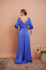 Vestido largo de satén color azul eléctrico, con escote en V cruzado, mangas 3/4 con lazos en los puños y tajo lateral alto.