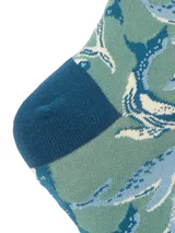 Calcetines largos de color verde azulado con estampado de ballenas en tonos azul y blanco. El talón y la puntera son de color azul oscuro. El borde superior es acanalado y tiene el logo de la marca.