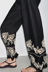 Pantalón culotte negro de lino y viscosa con bordados florales en el ruedo. Tiene tiro medio, cintura con trabillas, bolsillos laterales y cierre frontal con cremallera y botón.