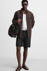 Bermuda regular fit negra confeccionada en tejido de lino. Cintura elástica ajustable con cordón y pliegues frontales. Bolsillos frontales y detalle de bolsillos traseros de plastrón.