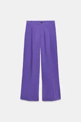 Pantalón de vestir color lila de tiro alto con pliegues frontales, corte palazzo, bolsillos laterales y cierre frontal con cremallera y botón.