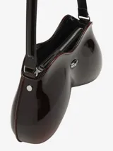 Bolso de hombro Diesel con forma orgánica y curvilínea, similar a un control de videojuegos. Acabado brillante, color negro con efecto degradado a gris oscuro en la parte inferior. Cuenta con un asa de hombro fina y un pequeño dije metálico con logo en el centro.