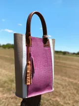 Bolso matero color fucsia con textura croco, laterales color beige con borde blanco y manijas de cuero marrón.