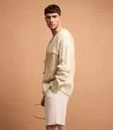 Cardigan de punto beige con diferentes texturas y bloques de color. Tiene cuello en V, abotonadura frontal y mangas largas.