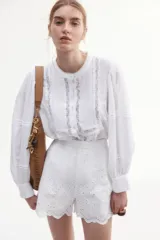 Blusa blanca de algodón con cuello mao, pechera con jaretas e inserciones de encaje, botones frontales, canesú fruncido en la espalda y mangas largas abullonadas con pinzas y abertura con botón en los puños.