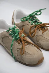 Zapatillas urbanas color marrón claro, confeccionadas en cuero, con cordones verdes y suela de goma.