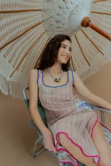 Vestido largo de tejido calado color beige, con estampado de flores en tonos rosados, celestes y verdes. Presenta escote cuadrado con ribete azul y terminaciones con crochet fucsia.