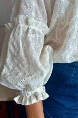 Camisa verde con rayas verticales blancas y bordados de flores. Tiene cuello mao, mangas largas abullonadas con puños elásticos y cierre frontal con botones de nácar.