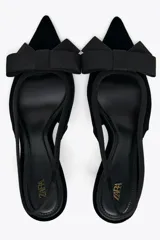 Zapato destalonado negro de terciopelo con tacón fino y tira trasera elástica. Detalle de lazo en la parte delantera.