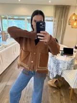 Cardigan marrón de punto con cuello en V, cierre frontal con botones, bolsillos de parche y flecos en el ruedo.