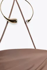 Vestido midi marrón de tejido de punto con escote recto y hombros descubiertos. Presenta detalle de collar metálico con aplicación de joyas, forro interior, bajo con abertura en la espalda, frunces en el tejido y cierre con cremallera oculta en la costura.
