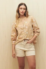 Camisa color beige con bordado floral blanco en toda la superficie. Presenta cuello mao, escote en V y abotonadura frontal, con mangas largas terminadas en puño angosto.