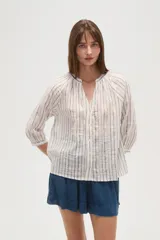 Camisa blanca de algodón con rayas verticales en tono beige/tostado y detalles de bordado tipo ojal a lo largo de las rayas. Presenta cuello mao con abertura en V y botones frontales, y mangas 3/4 con ligero volumen.