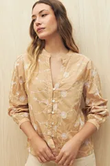 Camisa color beige con bordado floral blanco en toda la superficie. Presenta cuello mao, escote en V y abotonadura frontal, con mangas largas terminadas en puño angosto.
