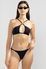 Conjunto de bikini negro con top halter con abertura en el centro y detalle de argolla dorada, y bombacha tipo colaless con tiras finas ajustables.
