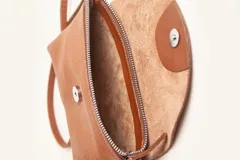 Cartera tipo sobre de cuero vacuno, con solapa frontal, cierre y broche magnético. Incluye correa larga ajustable y extraíble para usar como bandolera.