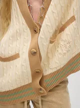 Cardigan largo color crema con detalles en color camel en el borde de los bolsillos, en el borde de los botones y en los puños. Tiene cuello en V y cierre con botones.