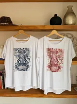 Remera blanca de algodón con cuello redondo y estampado de cerezas rojas con hojas verdes y texto dorado.