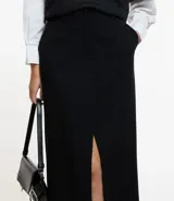 Falda midi de sastrería color negro, con trabillas en la cintura, cierre con botón y cremallera, y abertura delantera.
