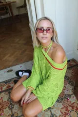 Vestido corto de punto calado color verde lima, con diseño de hombros caídos y detalles de rayas rojas en el escote y puños. Incluye un cordón tejido a juego con dijes de corazones dorados en los extremos que puede utilizarse como accesorio.