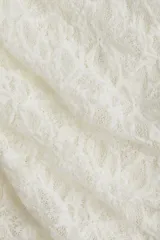 Pantalón largo de encaje blanco con corte acampanado y falda mini superpuesta con laterales fruncidos y cintura elástica.