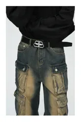 Pantalón de jean ancho (baggy) con lavado oscuro y efecto desgastado en tonos marrones/ocre. Presenta múltiples bolsillos cargo grandes con tapa y botones a presión en las piernas.